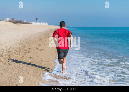 Rear view of man running on shore at beach Stock Photo