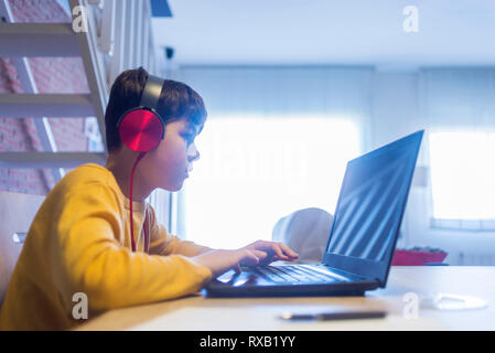 Side view of boy doing homework using headphones and laptop computer at home Stock Photo