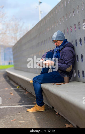 Fashionable senior man wearing warm clothing using tablet computer on seat in park during autumn Stock Photo