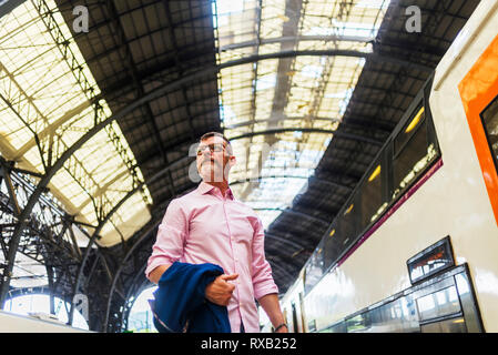 Low angle view of businessman looking away while standing at railroad station platform Stock Photo