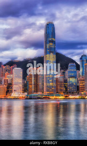 The tallest skyscraper tower on Hong Kong cityscape in Central CBD district against the tallest mountain on a cloudy morning when lights reflect in bl Stock Photo