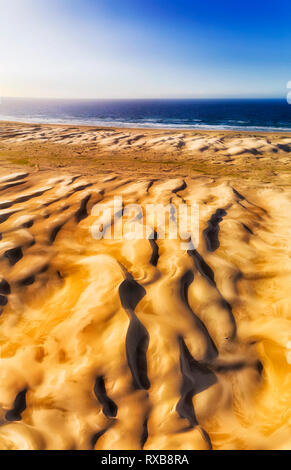 Polished and formed surface of Sand Dunes on Stockton beach facing Pacific ocean with strong winds in aerial vertical panorama from land to open sea a Stock Photo