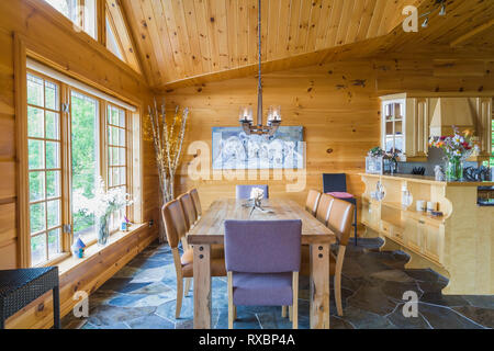 Oak wood table with caramel coloured high back leather chairs plus two high back end chairs with grey cloth upholstery and maple wood buffet in dining room with slate tile floor inside a piece sur piece Eastern white pine log and timber home, Quebec, Canada. This image is property released. CUPR0331