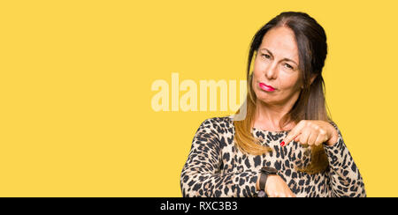 Beautiful middle age woman wearing leopard animal print dress In hurry pointing to watch time, impatience, upset and angry for deadline delay Stock Photo