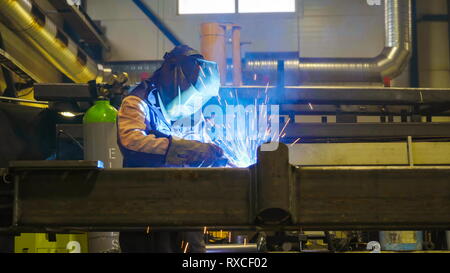 A man welding a metal sheet in the factory. The rays coming from the machine is bad for the eyes Stock Photo