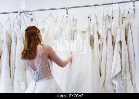 A pretty Red haired girl is Wedding Dress shopping by herself in a beautiful shop- she is trying on dresses and shoes Stock Photo
