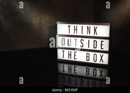 Think outside the box motivational message on a light box in a cinematic moody background Stock Photo