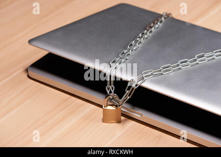 Heavy chain with a padlock around a laptop on table. Stock Photo