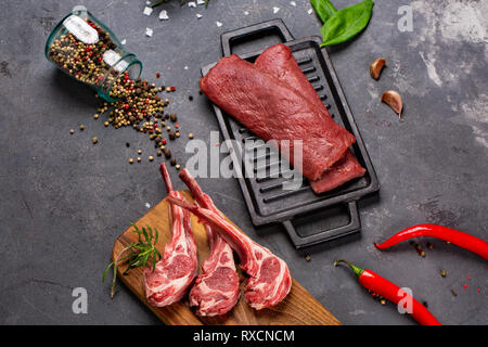 Set of Raw uncooked black angus beef tomahawk steaks on bones and veal tenderloin served with chilli and peppercorns. Rustic style. Close up Stock Photo