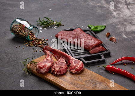 Set of Raw uncooked black angus beef tomahawk steaks on bones and veal tenderloin served with chilli and peppercorns. Rustic style. Close up Stock Photo
