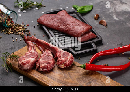 Set of Raw uncooked black angus beef tomahawk steaks on bones and veal tenderloin served with chilli and peppercorns. Rustic style. Close up Stock Photo