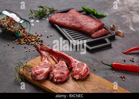 Set of Raw uncooked black angus beef tomahawk steaks on bones and veal tenderloin served with chilli and peppercorns. Rustic style. Close up Stock Photo