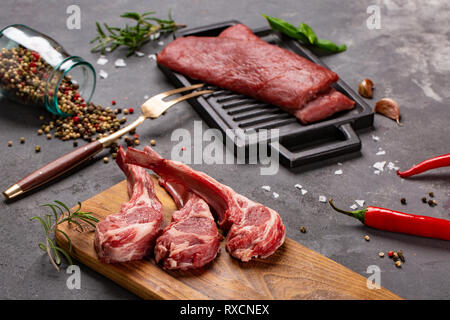 Set of Raw uncooked black angus beef tomahawk steaks on bones and veal tenderloin served with chilli and peppercorns. Rustic style. Close up Stock Photo