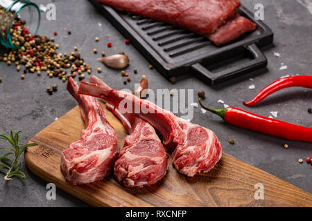 Set of Raw uncooked black angus beef tomahawk steaks on bones and veal tenderloin served with chilli and peppercorns. Rustic style. Close up Stock Photo