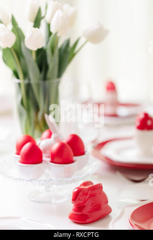 Happy easter. Decor and table setting of the Easter table is a vase with white tulips and dishes of red and white color. Easter colored eggs with whit Stock Photo