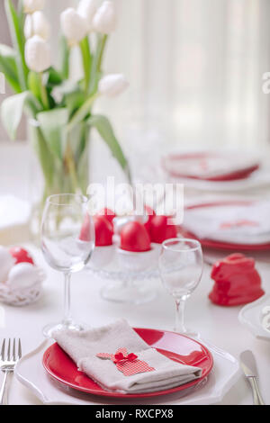 Happy easter. Decor and table setting of the Easter table is a vase with white tulips and dishes of red and white color. Easter colored eggs with whit Stock Photo