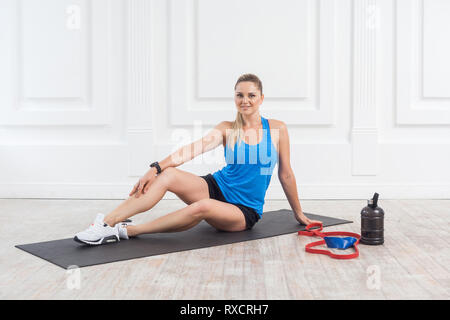 Happy satisfied beautiful young athletic causcasian woman in black shorts and blue top siting and have a rest after hard working on the gym. Indoor, s Stock Photo