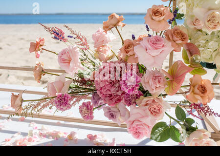 Part of the wedding arch decorated with fresh flowers is set on the sandy bank of the river. Wedding florist arranges workflow. Stock Photo