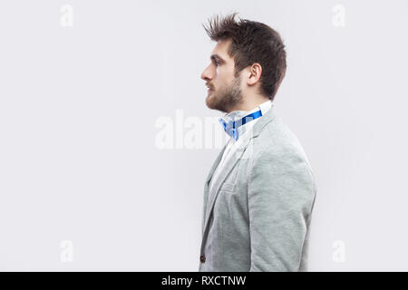 Profile side view portrait of serious handsome bearded man in casual grey suit, blue bow tie standing and looking straight wih calm serious face. indo Stock Photo