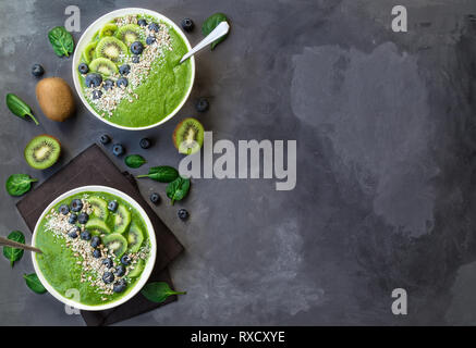 Breakfast green smoothie bowls with kiwi, blueberries and sunflower seeds on gray concrete background. Top view with space for text. Stock Photo