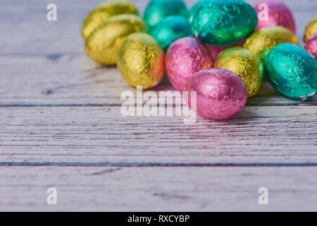 wrapped colored chocolate eggs against white wooden background with copy space, macro color photo Stock Photo