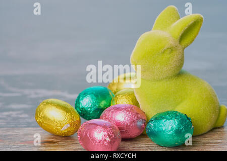green easter bunny with wrapped chocolate eggs against white wooden background with copy space Stock Photo