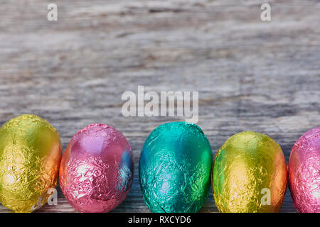 row with colorful chocolate eggs on a wooden brown background with copy space above as greeting card Stock Photo