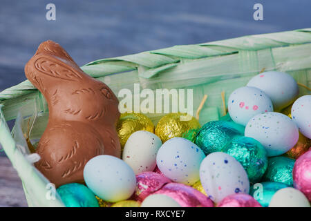 easter basket with a lot of colored chocolate easter eggs and dragee eggs with chocolate bunny on wooden background, macro photography Stock Photo