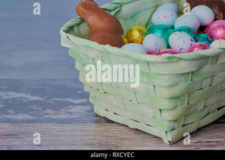 easter basket with a lot of colored chocolate easter eggs and dragee eggs with chocolate bunny on wooden background, macro photography Stock Photo