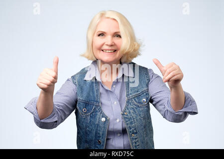 Smiling pretty senior woman showing double thumbs up. Positive human facial emotion Stock Photo