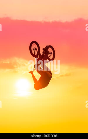 Silhouette of man performing tricks on bmx bike against pink sunset sky Stock Photo