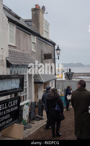 Lyme Regis, Dorset, UK. 9th March 2019. The Bell Cliff at the seaside resort town of Lyme Regis is transformed into a film set in readiness for the arrival of the cast and crew of historical drama Ammonite starring Kate Winslet and Saoirse Ronan. Widely anticipated to be a Hollywood blockbuster the fictional drama is inspired by the life of legendary fossil hunter Mary Anning and is a welcome boost for tourism and the local economy. Tourists look on as the set is consutructed. Credit: PQ Images/Alamy Live News Stock Photo