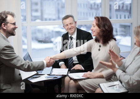 Smiling friendly businessman shaking hands with woman sitting at office desk Stock Photo