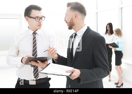 two employees discussing business documents in the office lobby. Stock Photo