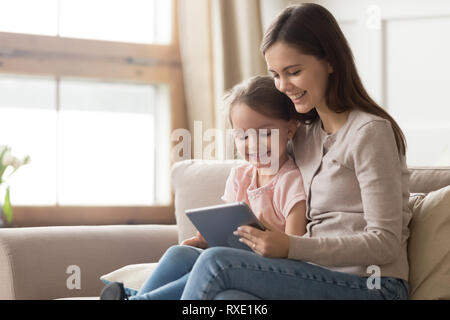 Happy mom and kid daughter using digital tablet on sofa Stock Photo