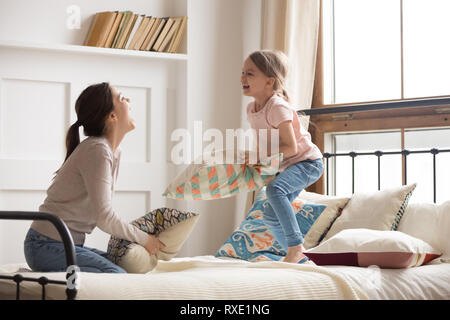 Happy mom and child girl enjoy pillow fight on bed Stock Photo