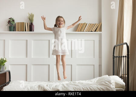 Happy funny child girl jumping on bed alone feeling joy Stock Photo