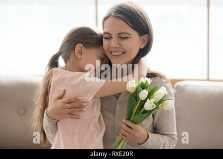 Kid daughter hugging mom holding tulips congratulating with mothers day Stock Photo