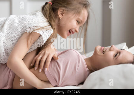 Happy kid and mother having fun laughing playing in bed Stock Photo
