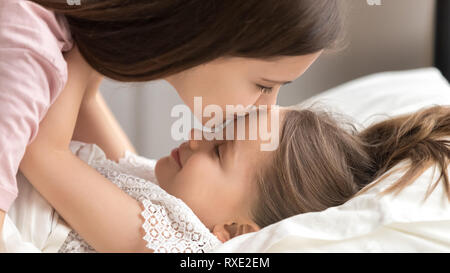 Loving mother kissing cute kid daughter waking up in morning Stock Photo