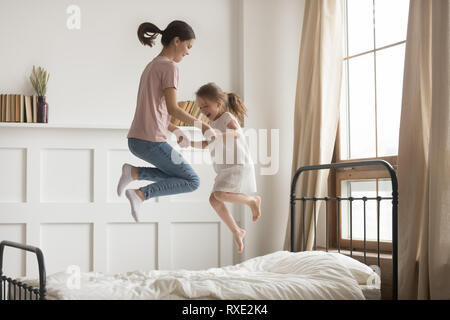 Happy mom and kid girl holding hands jumping on bed Stock Photo