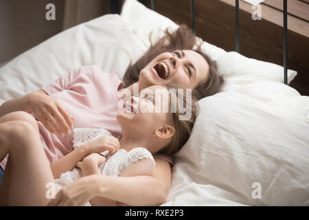 Happy family mother embracing kid daughter laughing lying on bed Stock Photo