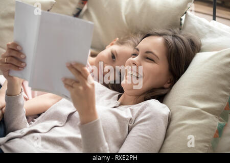 Happy mother and child daughter reading book laughing in bed Stock Photo
