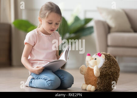 Cute little kid girl playing alone reading book to toy Stock Photo