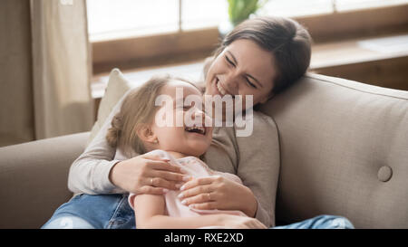 Happy mom embracing kid daughter laughing together lying on couch Stock Photo