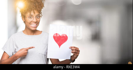 Young african american woman holding paper with red heart over isolated background very happy pointing with hand and finger Stock Photo