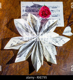 Still life composition made with a musical score folded in the shape of a flower and a red rose Stock Photo