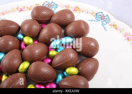 Chocolate easter eggs & colourful foil wrapped eggs on a white plate with a traditional flower design. Stock Photo