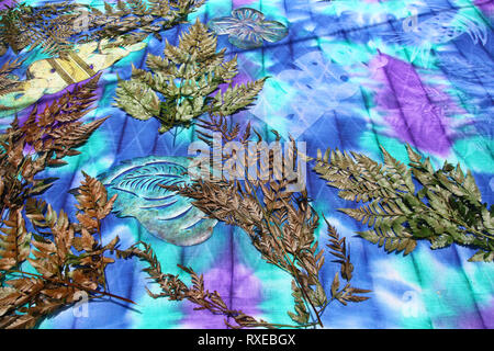 Colourful fabric with leaves, ferns & paper shapes cut out demonstraiting how to create tie dye designs, Bora Bora, French Polynesia. Stock Photo
