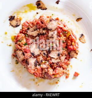top view of beef tartare with raw egg and truffle on white plate in Lombardy Stock Photo
